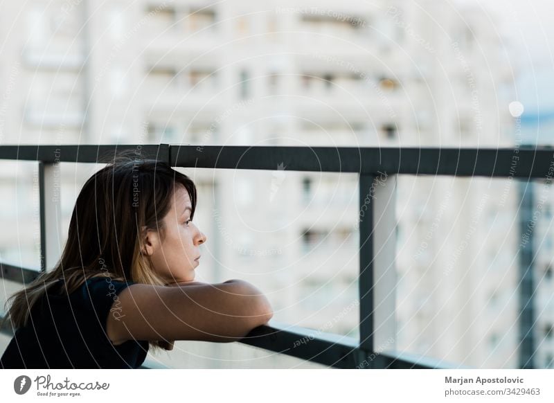 Young sad woman looking outside through balcony of an apartment building adult alone anxiety caucasian city concerned crisis depressed depression desperate