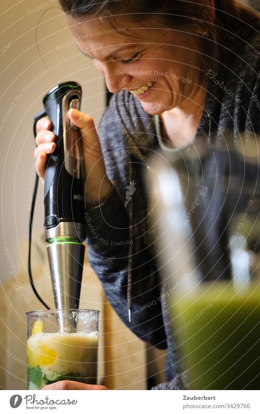 Pretty woman makes a smoothie with the hand blender and smiles Woman pretty already green salubriously Healthy Adults Human being Interior shot cake Glass