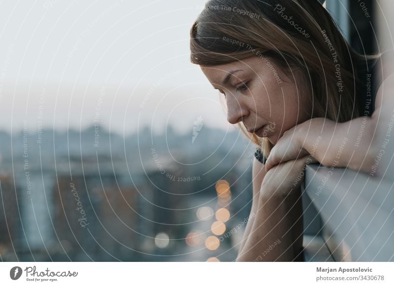 Young sad woman looking outside through balcony of an apartment building adult alone anxiety caucasian city concerned crisis depressed depression desperate