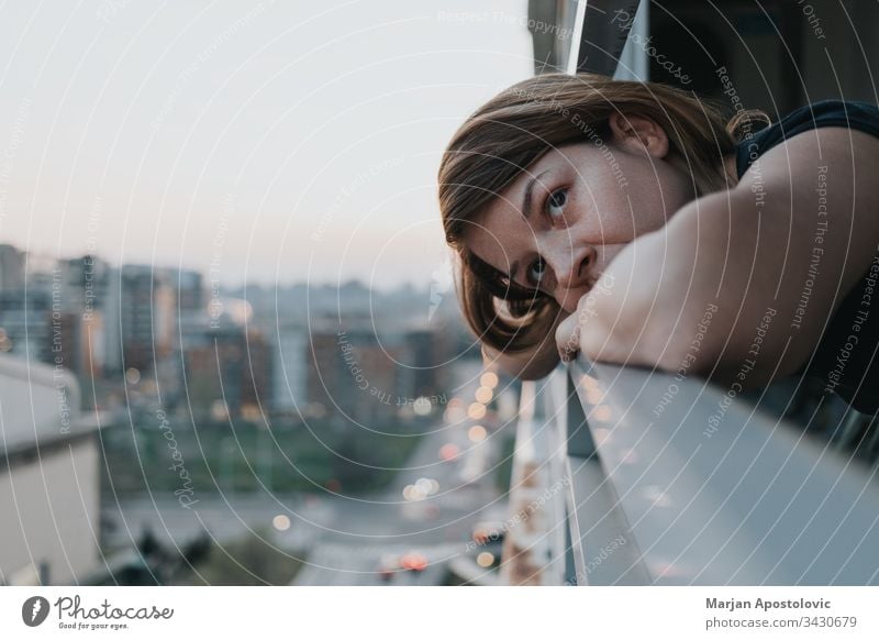 Young sad woman looking outside through balcony of an apartment building adult alone anxiety caucasian city concerned crisis depressed depression desperate