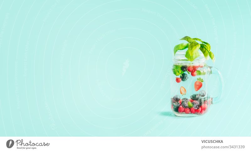 Berries detox fruit infused water in Mason jar flavored with herb leaves on table  at sunny turquoise blue background. Summer mood drinks and lifestyle. Healthy background