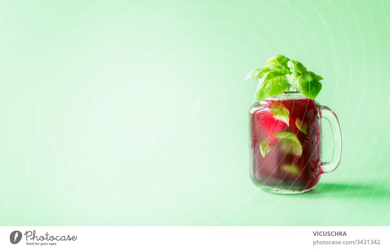 Red berries lemonade in Mason jar  flavored with herb leaves at sunny bight mint green background. Summer mood.  Healthy drinks and lifestyle. Copy space