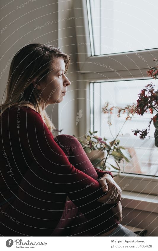 Young worried woman looking through the window adult alone anxious apartment caucasian covid19 depressed depression displeased distancing distant expression