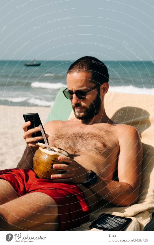 Stranded man on vacation sitting on the beach with a coconut in one hand and is busy with his smartphone Holidaymakers Beach travel Tourist Coconut stressed