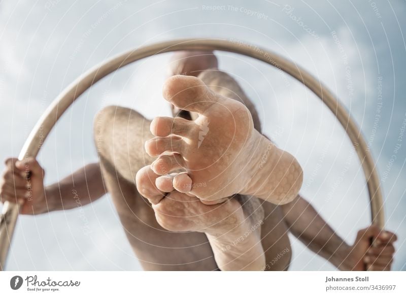 Gymnastic man with ring from below in front of blue sky Ring Man Body Arm hands feet Toes Knee Gymnastics Acrobatics stop Sky Clouds Circle Chrome