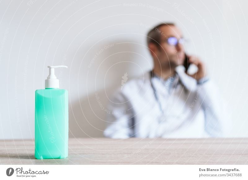 doctor man using mobile phone. Front focus on an alcohol gel or antibacterial disinfectant. Hygiene and corona virus concept. Covid-19 professional hospital