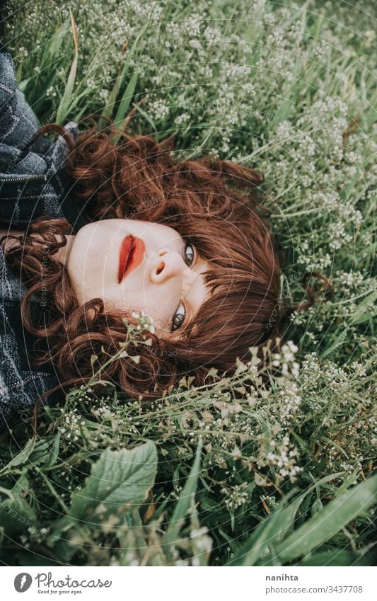 Young beautiful woman resting in a field of flowers portrait mood spring dark romantic nostalgia emotions green brunette pretty face white caucasian nature