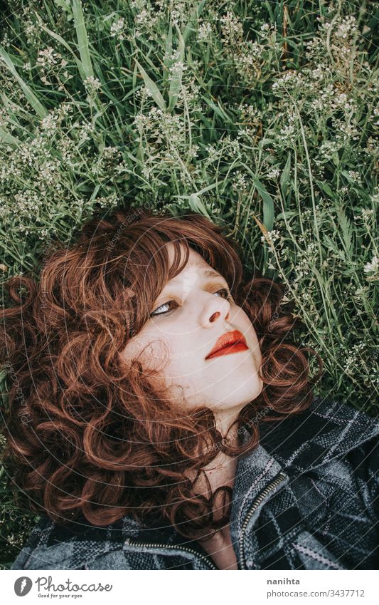 Young beautiful woman resting in a field of flowers portrait mood spring dark romantic nostalgia emotions green brunette pretty face white caucasian nature