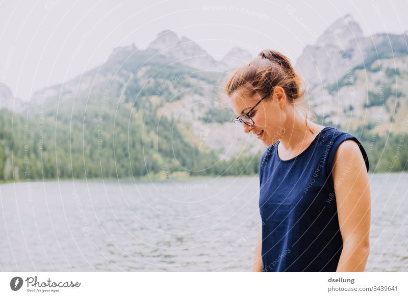 young woman looks smiling on the ground in front of a lake with peaks in the background Youth (Young adults) luminescent Attractive 1 Person youthful Adults