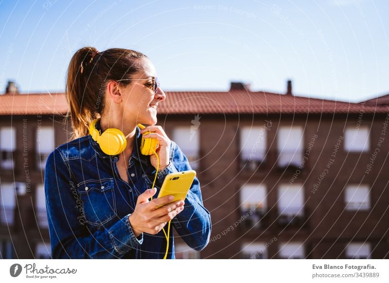 young woman listening to music on mobile phone and yellow headset. Fun and lifestyle technology fun terrace outdoors sunny sunglasses happy caucasian active