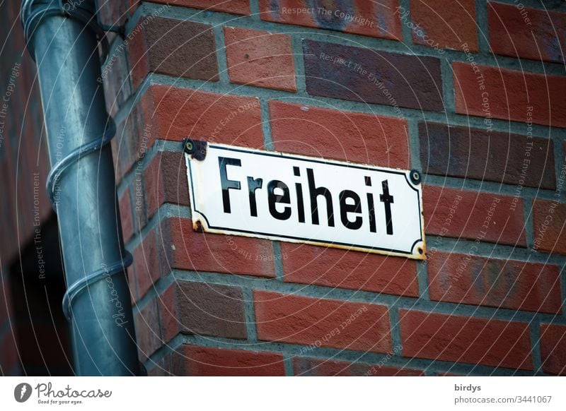 Freedom, street sign on a brick facade. Word freedom as a symbol for the most important good in a democracy. Current restrictions of freedom of movement and action in the Corona crisis. Longing for universal freedom