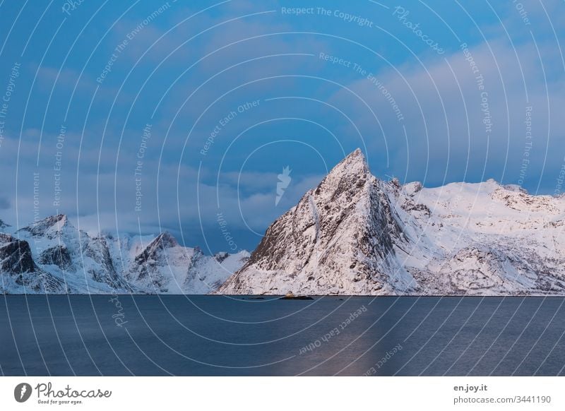 Snowy mountains by the fjord Sunset Shadow Light and shadow cloudy Wide angle Peak Island Clouds Sky North Relaxation Winter vacation Ocean Environment