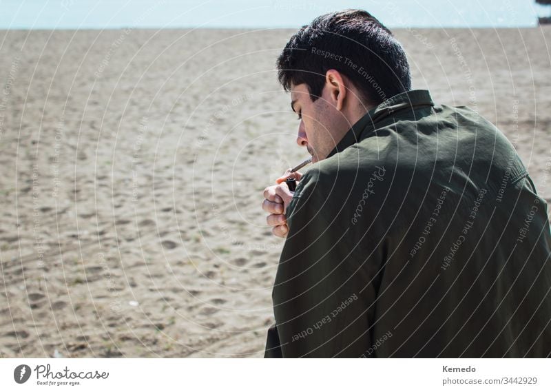 Young man smoking a marijuana joint or cigarette on the beach during a sunny day. Blur background and copy space left. person people cannabis smoke weed young