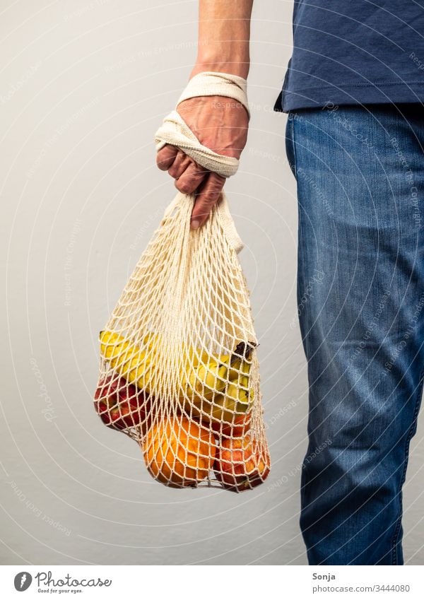 Mann hält wiederverwendbare Tasche mit frischen Obst in seiner Hand, gesunde Ernärhung, plastikfrei einkaufen fruit Banane orange apfel Fresh Vitamin