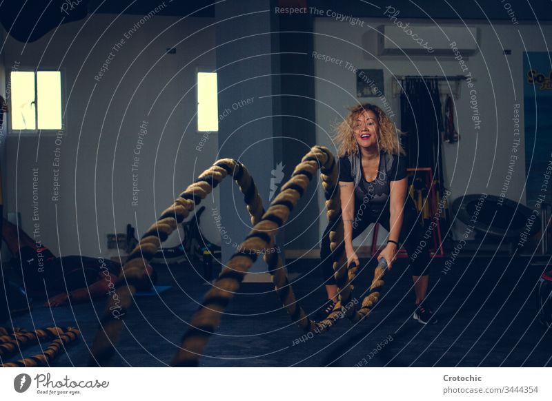 Blonde woman using the battle rope in a gym sport aerobics athlete club determination effort endurance exercise fit fitness gymnastics heavy improvement