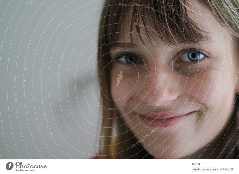 Female, happy teenager with blue eyes and pony, smiles positively, happily and optimistically with smiling mouth and joy of life, in front of a grey background, into the day.