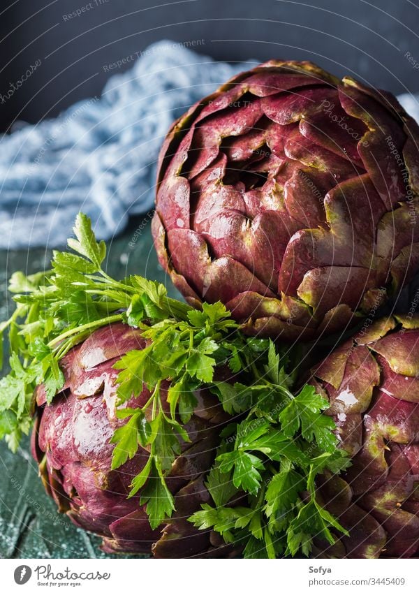 Raw artichokes with parsley on dark background raw uncooked drop water vegetable food vegetarian herb ingredient closeup green texture color italian