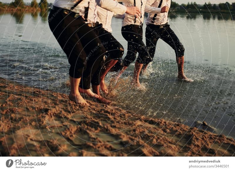 Men's feet in the water. men in costumes run on water. They are having fun, playing and splashing water around them. summer. group of happy young man feet splash water in sea and spraying at the beach