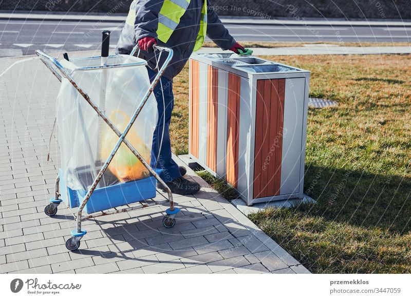 Cleaning service worker emptying the trash. Man wearing yellow vest, cleaning a bin, standing beside a cleaning cart. Real people, authentic situations plastic