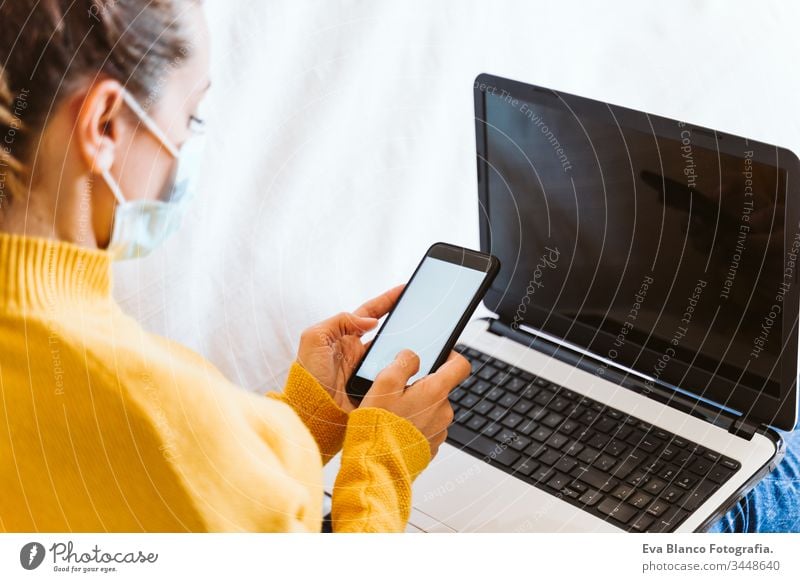 young woman working on laptop at home, sitting on the couch, wearing protective mask. Stay home concept during coronavirus covid-2019 pandemic stay home