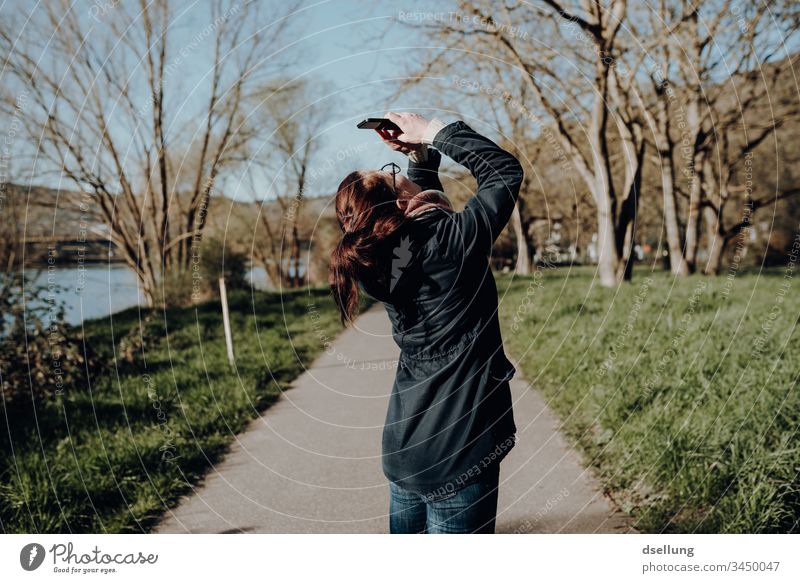 Young woman in nature takes pictures with her smartphone, holding her back in a position that brings sweat stains under the armpits of every orthopaedic surgeon