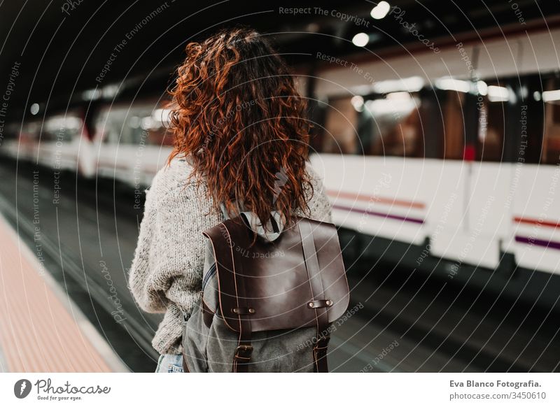 young beautiful woman at train station using mobile phone before catching a train. Back view. Travel, technology and lifestyle concept travel moving caucasian