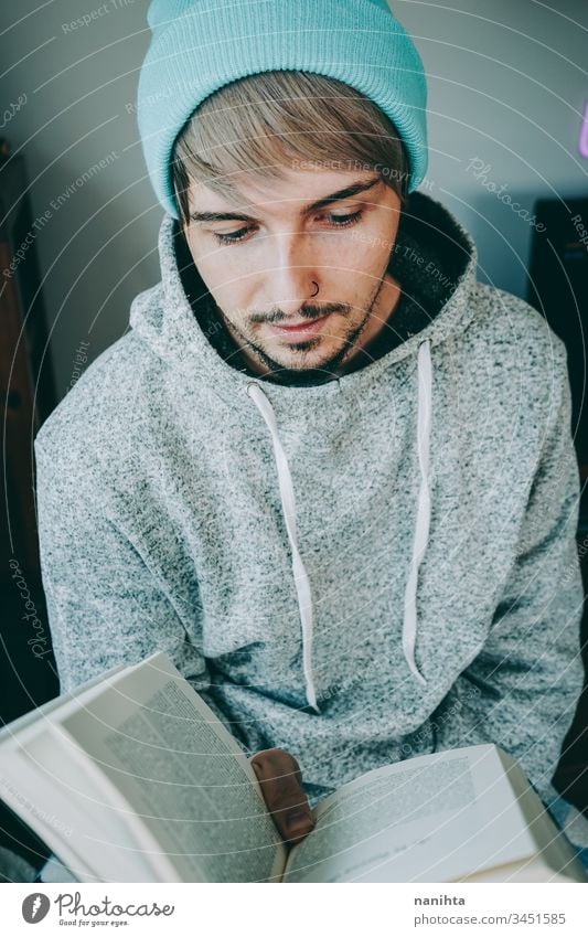 Young man reading a book in his home attractive quarantine hobby leisure relax enjoying learn study student young youth indoors room decoration life casual real