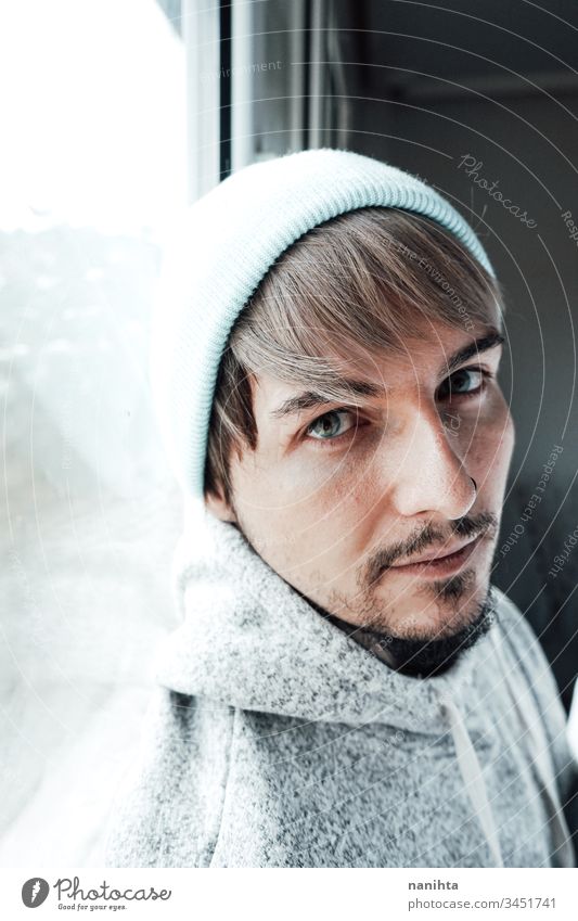 Young man alone in his home near a window male portrait isolated locked quarantine lonely self attractive handsome guy casual wear hairstyle blue eyes lenses