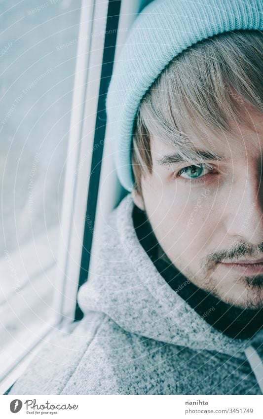 Young man alone in his home near a window male portrait isolated locked quarantine lonely self attractive handsome guy casual wear hairstyle blue eyes lenses