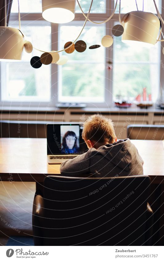 Little boy, schoolchild at home, in video chat with his teacher, at the dining table in front of the window Child Schoolchild Notebook Table Dinner table