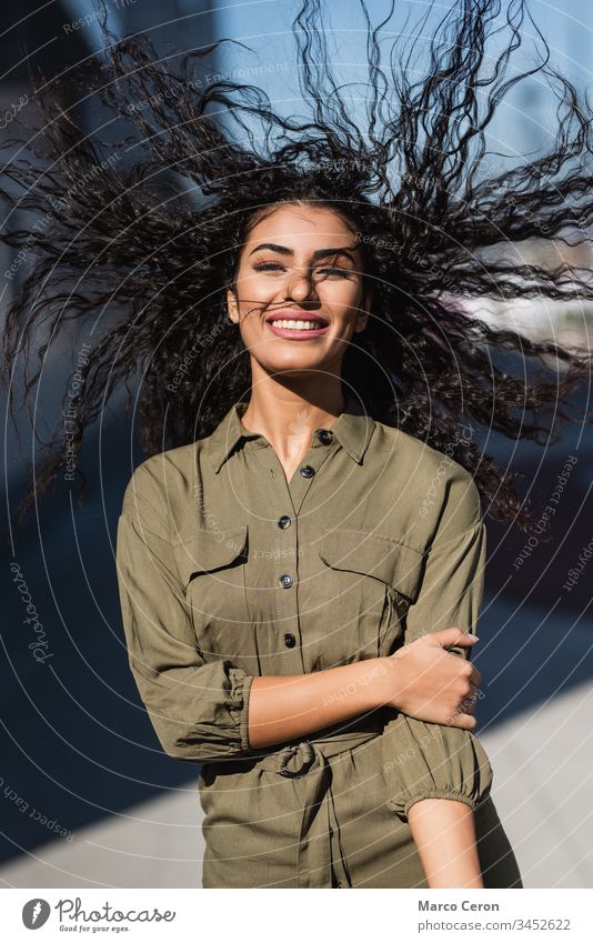 Young attractive woman with her wavy hair in the wind smiling portrait cheerful young adult front view fun looking at camera outdoors blowing happiness