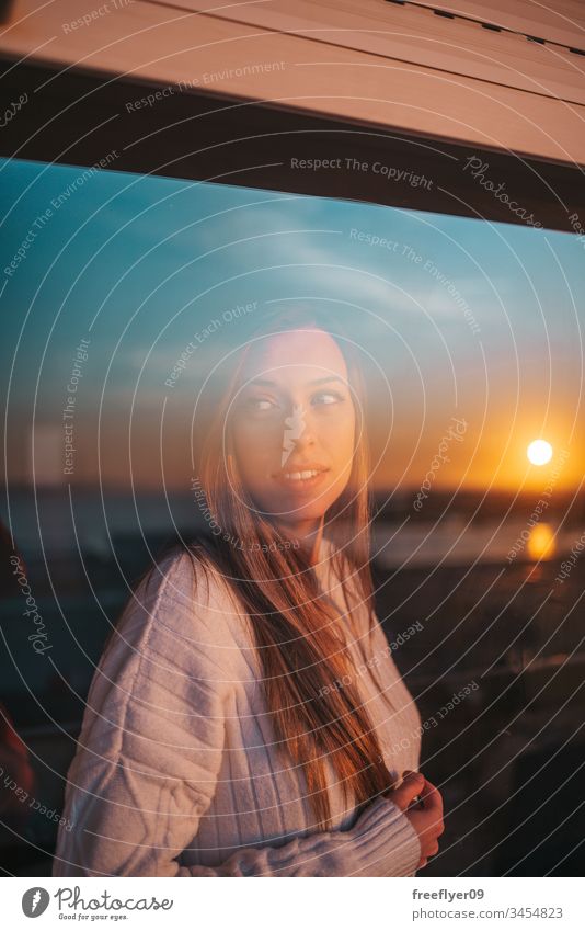 Young woman behind a window quarantine self-isolation glass reflection sunset barrier coronavirus covid19 covid-19 orange white black blue contemplating