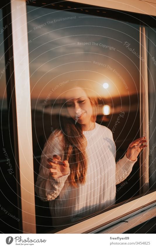 Young woman behind a window quarantine self-isolation glass reflection sunset barrier coronavirus covid19 covid-19 orange white black blue contemplating