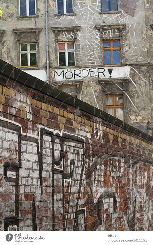 Murderer, standing in black letters, as lettering, on an old squat house, with many windows, behind a brick wall painted with graffiti. Sign as an appeal against racism, war, hatred, violence, brutality and discrimination.