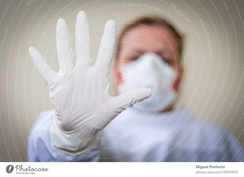 Nurse with protective mask and outstretched hand with a glove on advising to keep the safe distance so as not to get infected on a beige background doctor