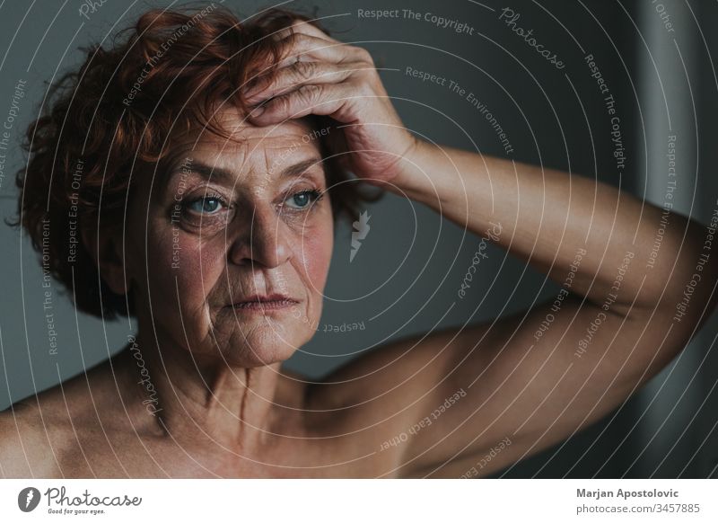 Mature woman by the window thinking about life 60s adult age aged aging alone beautiful care caucasian close-up contagion contemplating depression elder elderly