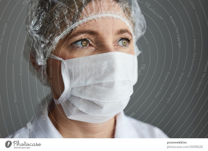 Doctor with face covered with mask. Portrait of young woman wearing the uniform, cap and mask to avoid virus infection and to prevent the spread of disease. Real people, authentic situations