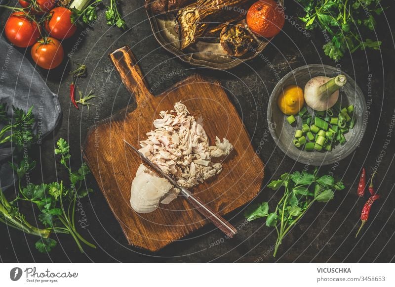 Pulled chicken breast on cutting board with knife with vegetables ingredients on dark rustic background. Top view. Healthy food eating. Low carb fitness dieting. Easy cooking