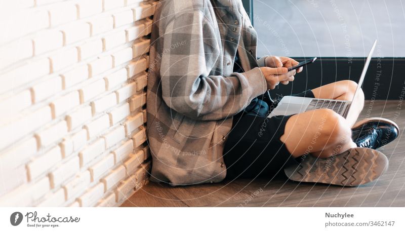 Young millennial man sitting on floor and learning online class from smartphone and laptop in his home during self quarantine from pandemic of Covid-19 and coronavirus