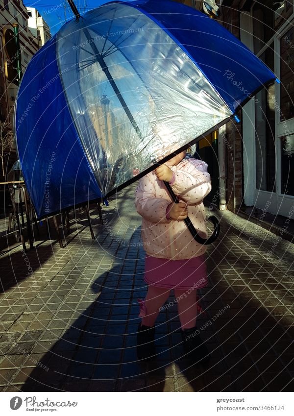 Little girl with big umbrella against the sun in the street. Child loves to hide under child kid toddler autumn outside fall lady playful weather city people