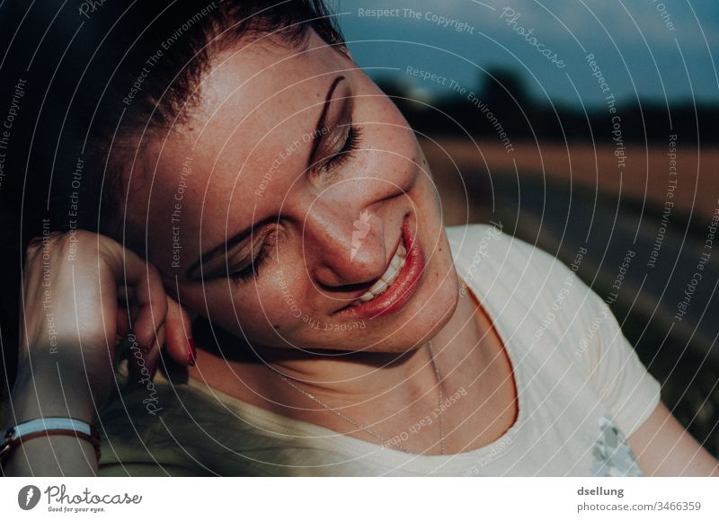 Young woman sitting smiling and relaxed on a bench in the evening light Weather Interest Curiosity Life Inspiration Upper body Portrait photograph Contrast