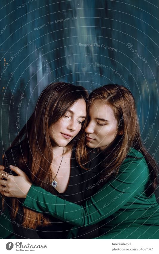 Two young adult sisters or friends sitting and hugging with eyes closed, selective focus asian attractive beautiful caucasian couple family fashion female girl