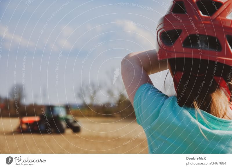 Girl with red bicycle helmet watches tractor in the field Träcker Tractor bulldog Agriculture Field Colour photo Exterior shot Work and employment Nature