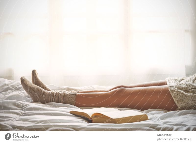 Soft photo of woman legs on the bed with old book next her read reading window view lazy sunday winter coffee cup tea morning girl home relax socks beautiful