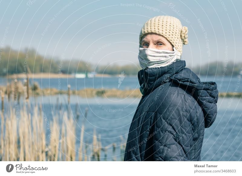 A poor elderly woman wears a homemade mask to protect herself from viruses adult bench breathing coat contagion contagious corona coronavirus cough country