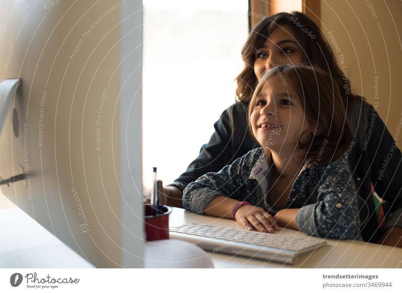 Mom and daughter at the computer mother home family child woman parent girl technology mom female happy people smiling teaching adult using working internet