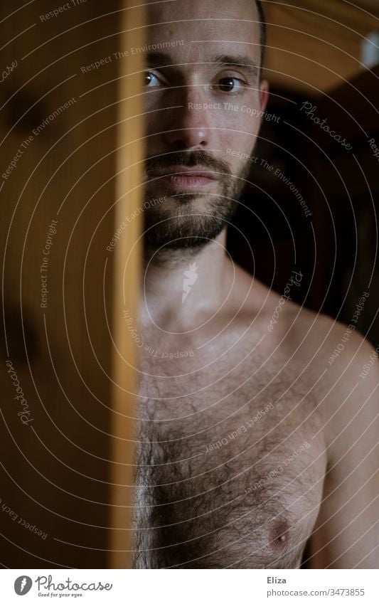 A man with naked upper body, looking out behind a wooden door directly into the camera Man Upper body free Chest Naked Wooden door look into the camera