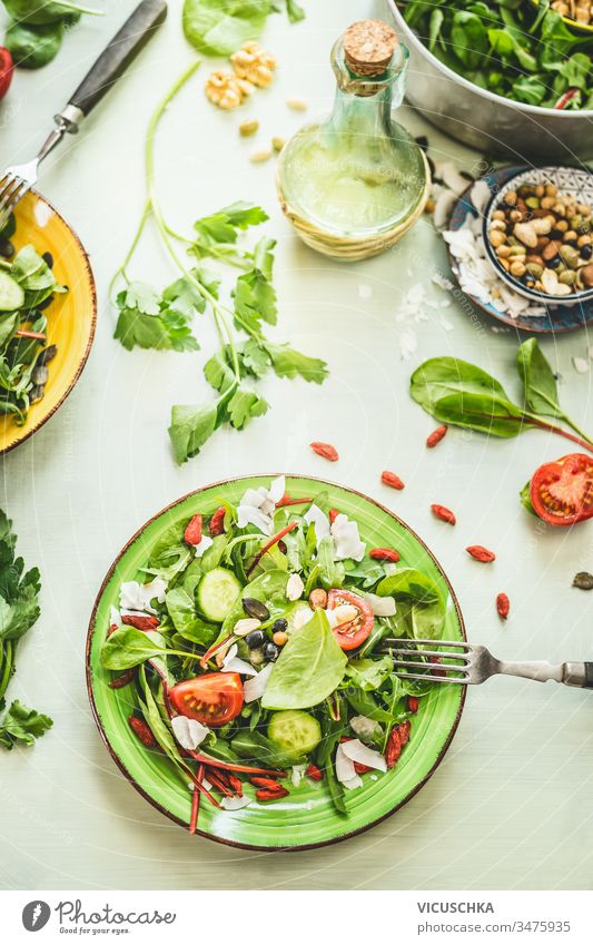 Healthy fresh green salad plate topped with various seeds and berries on light table background with olives oil and ingredients. Top view healthy top view above