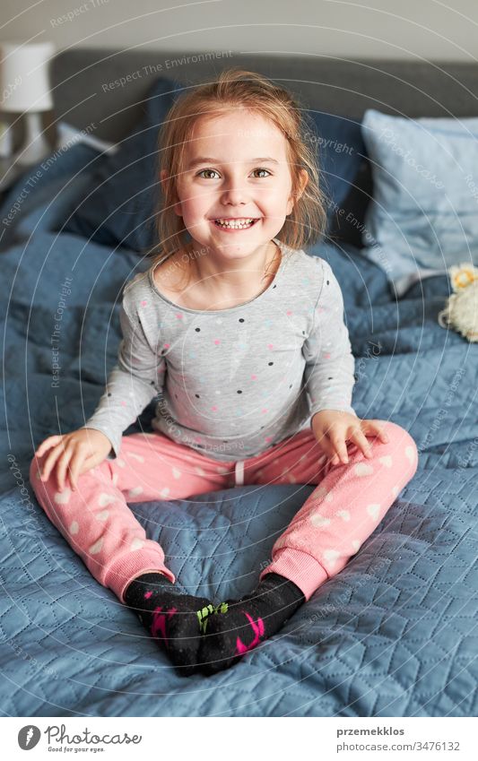 Little happy playful kid girl having fun making silly funny faces jumping on bed in bedroom in the morning at home playing childhood joy cute laughing smiling