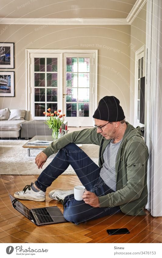 HomeOffice: relaxed man sitting on the floor in front of his notebook and drinking coffee Living room Home office Man Only one man Mid adult man Eyeglasses